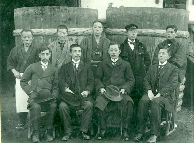 Chikashi Kanomata, engineer of the Brewing Research Institute by the Ministry of Finance (front row, center right); Assistant Professor Hitoshi Matsumoto, Kyoto Imperial University (front row, center left); Tsunekichi Okura, Gekkeikan’s 11th head (front row, farthest right); Yoshitoki Miyakoshi (back row, center; one who taught Western-style bookkeeping to Tsunekichi); Kisaburo Nonoguchi, chief sake brewer (back row, farthest left)